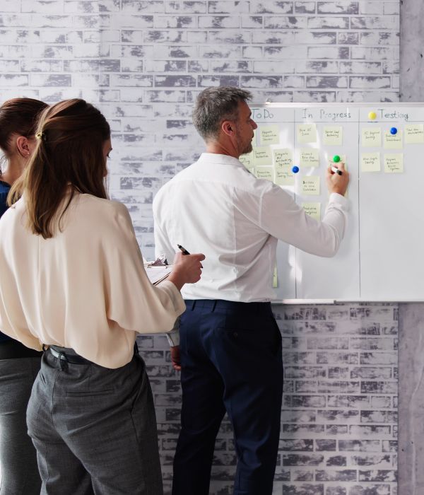 Team standing at a white board with sticky notes outlining what stage of the process each task is in