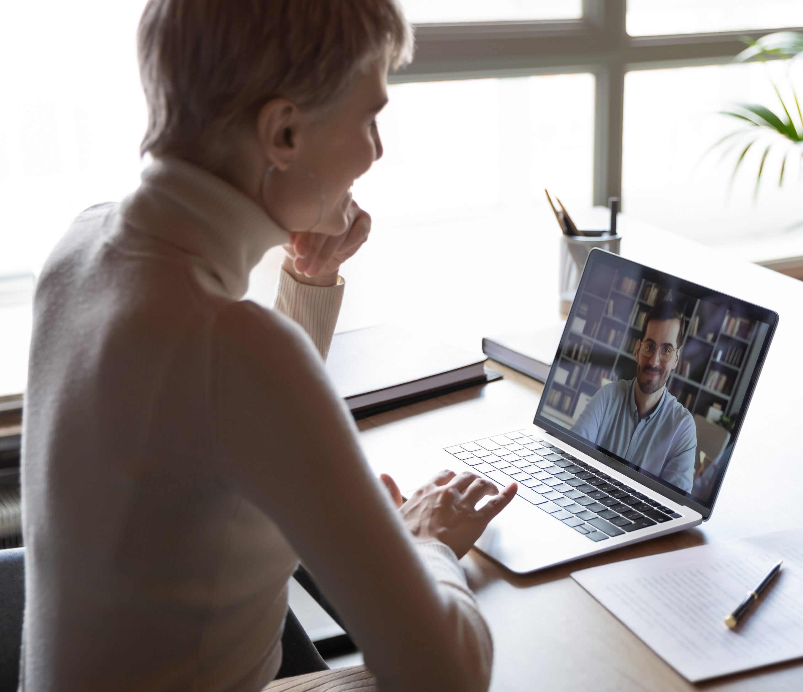 View over shoulder of a woman virtually interviewing a man on a laptop