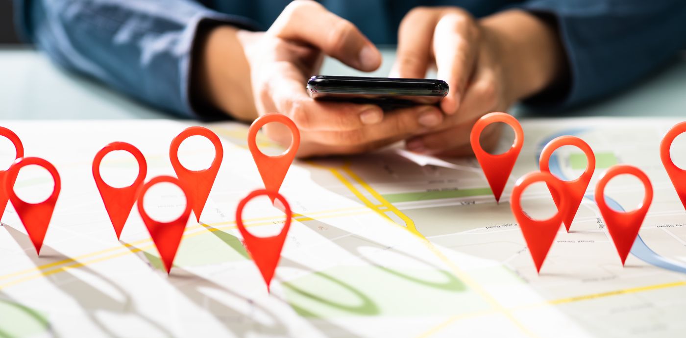 Image of person using a mobile phone with location pins on a map on the desk