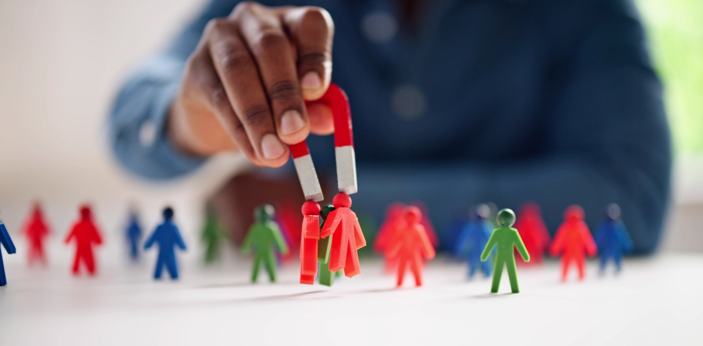 Person holding a magnet over toy figures of people